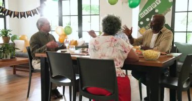 Bir grup mutlu üst düzey çok ırklı, beyaz ve siyah erkek ve kadın arkadaşlar oturma odasındaki emeklilik partisinde kadeh kaldırıyorlar. Kutlama, emeklilik, parti, son sınıf yaşam tarzı ve arkadaşlık kavramı.