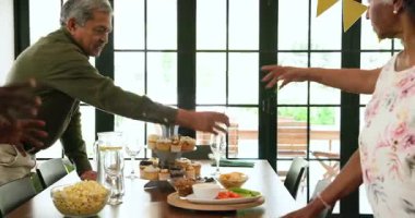 Bir grup mutlu üst düzey çok ırklı, beyaz ve siyah erkek ve kadın arkadaşlar oturma odasındaki emeklilik partisinde masa hazırlıyorlar. Kutlama, emeklilik, parti, son sınıf yaşam tarzı ve arkadaşlık kavramı.