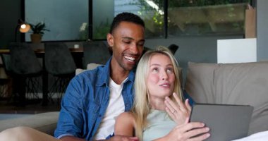 Mutlu siyah adam ve beyaz bayan partneri gülümsüyor ve nişan yüzüklerini evdeki tablet görüntülü sohbette gösteriyorlar. İletişim, ilişki, aşk, mutluluk, yaşam tarzı ve ilişki kavramı.