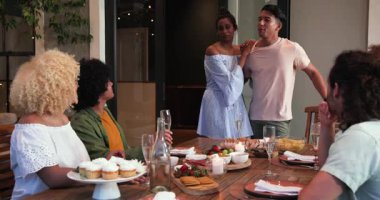 Ayakta duran ve tost içen mutlu çift, çeşitli arkadaşlar masada otururken kutluyor. Kutlama, akşam yemeği, yaşam tarzı ve arkadaşlık konsepti.