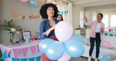 Üç mutlu çok ırklı ve beyaz bayan arkadaş balon asıp güneşli oturma odasında bebek partisine hazırlanıyor. Kutlama, annelik, parti, yaz ve arkadaşlık kavramı.