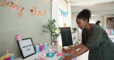 İki mutlu çok ırklı ve siyah bayan arkadaş güneşli oturma odasında bebek partisi için yemek ve dekorasyon hazırlıyorlar. Kutlama, annelik, parti, yaz ve arkadaşlık kavramı.