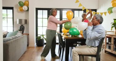 Oturma odasındaki bir doğum günü partisinde balon şişiren üst düzey çok ırklı ve beyaz erkek ve kadın arkadaşlar grubu. Kutlama, doğum günü, parti, son sınıf yaşam tarzı ve arkadaşlık konsepti.