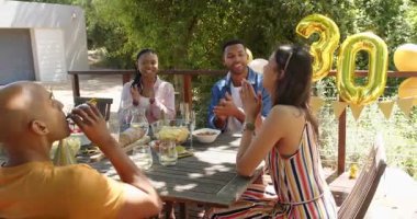 Bir grup mutlu çok ırklı ve siyah erkek ve kadın arkadaş güneşli bir günde bahçede kutlama yapıyor ve kadeh kaldırıyor. Kutlama, doğum günü, parti, yaz ve arkadaşlık kavramı.