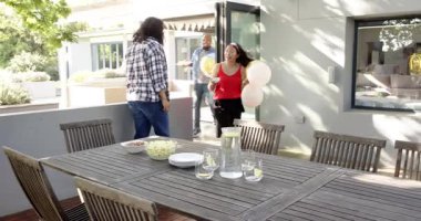 Bir grup mutlu, çok ırklı, siyah ve Çinli erkek ve kadın arkadaş terasta bir doğum günü partisi için sofra ve dekorasyon hazırlıyorlar. Kutlama, doğum günü, parti, yaz ve arkadaşlık kavramı.