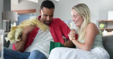 Mutlu siyah adam ve beyaz bayan partneri oturma odasında balonlarla süslenmiş doğum günü hediyesini açıyorlar. Parti, doğum günü, eğlence, eğlence, aşk, mutluluk, yaşam tarzı ve ilişki konsepti.