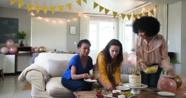 Üç mutlu, çok ırklı ve beyaz bayan arkadaş. Güneşli oturma odasındaki bir doğum günü partisinde abur cubur yiyip sohbet ediyorlar. Kutlama, doğum günü, parti, yaz ve arkadaşlık kavramı.