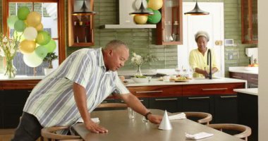 Mutfaktaki yemek masasını balonlarla süslenmiş mutlu kıdemli çift. Yaşlılık, ev hayatı, aşk, mutluluk, yaşam tarzı ve ilişki konsepti.