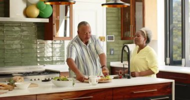 Mutlu kıdemli çift gülümseyerek, konuşarak ve mutfakta balonlarla süslenmiş şekilde yemek yiyerek. son sınıf, ev hayatı, aşk, mutluluk, yaşam tarzı ve ilişki konsepti.