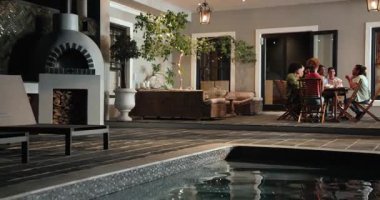 Yüzme havuzunu geçtikten sonra terasta sohbet eden mutlu arkadaşlara doğru çekim yapmak. Kutlama, akşam yemeği, yaşam tarzı, birliktelik ve arkadaşlık konsepti.