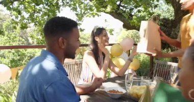 Bir grup mutlu çok ırklı ve zenci erkek ve kadın arkadaş güneşli bir günde bahçedeki bir doğum günü partisinde hediye veriyorlar. Kutlama, doğum günü, parti, yaz ve arkadaşlık kavramı.