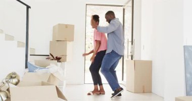 Mutlu siyah çift eve giriyor, birlikte dans ediyorlar, el ele tutuşuyorlar ve gülümsüyorlar, salondaki kutularla. Taşınmak, ilişki ve yaşam tarzı kavramı.