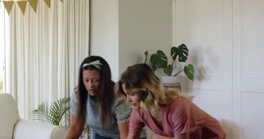 İki mutlu çok ırklı ve beyaz bayan arkadaş güneşli oturma odasında bir doğum günü partisi için masayı hazırlıyorlar. Kutlama, doğum günü, parti, yaz ve arkadaşlık kavramı.