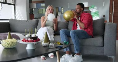 Mutlu siyah adam ve beyaz bayan partneri konuşuyor, balon şişiriyor ve ev partisi için dekorasyon odası hazırlıyorlar. Parti, doğum günü, eğlence, eğlence, aşk, mutluluk, yaşam tarzı ve ilişki konsepti.