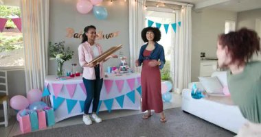 Üç mutlu çok ırklı ve beyaz bayan arkadaş güneşli oturma odasındaki bir bebek partisinde oyun oynayıp tahtaya yazı yazıyorlar. Kutlama, annelik, parti, yaz ve arkadaşlık kavramı.