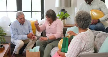 Bir grup mutlu üst düzey çok ırklı, beyaz ve siyah erkek ve kadın arkadaş oturma odasındaki bir doğum günü partisinde hediye veriyorlar. Kutlama, doğum günü, parti, son sınıf yaşam tarzı ve arkadaşlık konsepti.