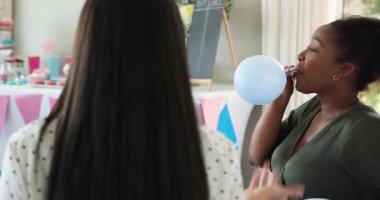 İki mutlu çok ırklı ve siyah bayan arkadaş balonları şişirip güneşli oturma odasında bebek partisine hazırlanıyor. Kutlama, annelik, parti, yaz ve arkadaşlık kavramı.