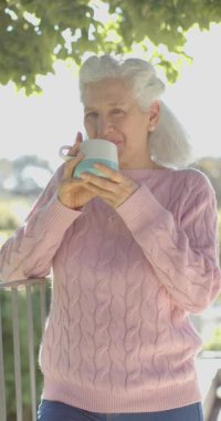 Kafkas kadının balkonda kahve içtiği dikey video, yavaş çekim. Ev hayatı, emeklilik ve yaşam tarzı, değişmedi..