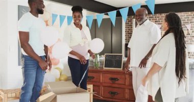 Cinsiyet teşhisi, mutlu siyah çift ve yaşlı ebeveynler bebek partisinde balonlu kutuyu açıyorlar. Kutlama, ebeveynlik, parti ve aile kavramı.