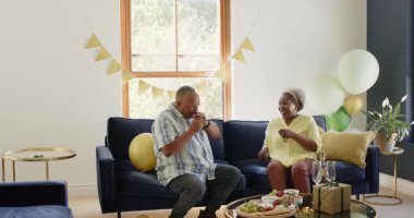 Mutlu kıdemli çift, oturma odalarını parti için hazırlıyorlar, balonlarla dekore ediyorlar. Parti, kutlama, yaşlılık, aşk, mutluluk, yaşam tarzı ve ilişki konsepti.