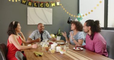 Bir grup mutlu, çok ırklı, siyah ve Çinli erkek ve kadın arkadaş masada oturmuş, oturma odasındaki yeni ev partisi için kadeh kaldırıyorlar. Kutlama, parti, yaz ve arkadaşlık konsepti.