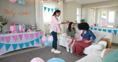 Üç mutlu çok ırklı ve beyaz bayan arkadaş güneşli oturma odasındaki bir bebek partisinde göbek ve tahtaya yazı yazıyorlar. Kutlama, annelik, parti, yaz ve arkadaşlık kavramı.