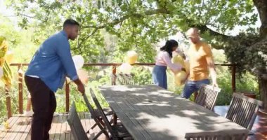 Mutlu çok ırklı ve siyah erkek ve kadın arkadaşlar güneşli bir günde bahçede doğum günü partisi için masa ve dekorasyon hazırlıyorlar. Kutlama, doğum günü, parti, yaz ve arkadaşlık kavramı.