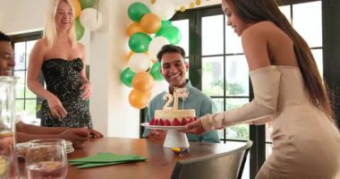 Bir grup mutlu, çok ırklı, beyaz ve Hintli erkek ve kadın arkadaşlar güneşli oturma odasındaki bir doğum günü partisinde pastaya mum üflüyorlar. Kutlama, doğum günü, parti, yaz ve arkadaşlık kavramı.