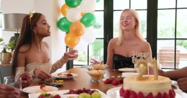 Bir grup mutlu, çok ırklı, beyaz ve Hintli erkek ve kadın arkadaş güneşli oturma odasındaki bir doğum günü partisinde konuşuyorlar ve kadeh kaldırıyorlar. Kutlama, doğum günü, parti, yaz ve arkadaşlık kavramı.