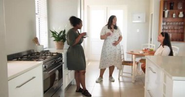 Üç mutlu çok ırklı ve siyah bayan arkadaş çay içip güneşli mutfakta hamileliklerini ilan ediyorlar. Kutlama, annelik, parti, yaz ve arkadaşlık kavramı.