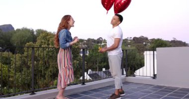 Mutlu adam diz çöküp, ortağına çatıda kalp balonlarıyla evlenme teklif ediyor. Nişan, aile hayatı, aşk, mutluluk, yaşam tarzı ve ilişki kavramı.