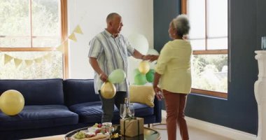 Mutlu kıdemli çift, parti için oturma odası hazırlıyorlar, balonlarla dekore ediyorlar, dans ediyorlar. Parti, kutlama, yaşlılık, aşk, mutluluk, yaşam tarzı ve ilişki konsepti.