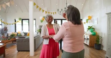 Bir grup mutlu üst düzey çok ırklı, beyaz ve siyah erkek ve kadın arkadaş oturma odasındaki bir doğum günü partisinde kutlama yapıyorlar. Kutlama, doğum günü, parti, son sınıf yaşam tarzı ve arkadaşlık konsepti.