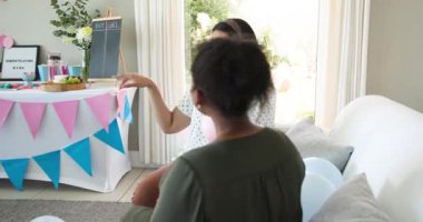 İki mutlu çok ırklı ve siyah bayan arkadaş balonları şişirip güneşli oturma odasında bebek partisine hazırlanıyor. Kutlama, annelik, parti, yaz ve arkadaşlık kavramı.