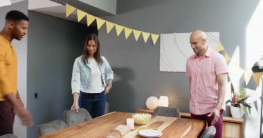 Bir grup mutlu çok ırklı ve siyah erkek ve kadın arkadaş oturma odasındaki bir doğum günü partisinde masada oturuyorlar. Kutlama, doğum günü, parti, yaz ve arkadaşlık kavramı.