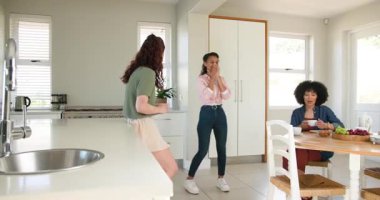 Üç mutlu çok ırklı ve beyaz bayan arkadaş çay içiyor, konuşuyor ve güneşli bir mutfakta bebek partisinde kucaklaşıyorlar. Kutlama, annelik, parti, yaz ve arkadaşlık kavramı.