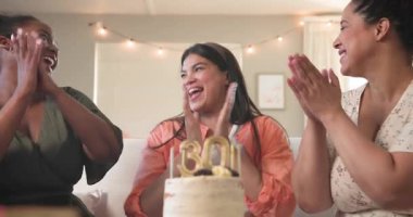 Üç mutlu çok ırklı ve siyah bayan arkadaş güneşli oturma odasındaki bir doğum günü partisinde pastaya mum üflüyorlar. Kutlama, doğum günü, parti, yaz ve arkadaşlık kavramı.