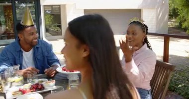 Güneşli bir günde, bahçedeki bir doğum günü partisinde hediyeleri açan bir grup mutlu çok ırklı ve siyah erkek ve kadın arkadaş. Kutlama, doğum günü, parti, yaz ve arkadaşlık kavramı.