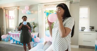 İki mutlu çok ırklı ve siyah bayan arkadaş balonları şişirip güneşli oturma odasında bebek partisine hazırlanıyor. Kutlama, annelik, parti, yaz ve arkadaşlık kavramı.