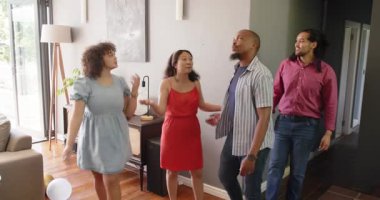 Bir grup mutlu, çok ırklı, siyah ve Çinli erkek ve kadın arkadaş eve girer ve oturma odasındaki hoş geldin partisinde masaya otururlar. Kutlama, parti, yaz ve arkadaşlık konsepti.