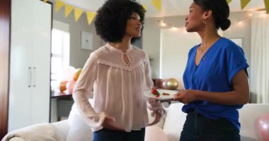 Güneşli oturma odasındaki bir doğum günü partisinde konuşan ve hazırlanan üç mutlu çok ırklı ve beyaz bayan arkadaş. Kutlama, doğum günü, parti, yaz ve arkadaşlık kavramı.