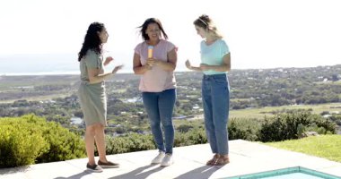 Üç mutlu çok ırklı ve beyaz bayan arkadaş güneşli bir günde terasta bir bebek partisinde işaret fişeği yakıyor. Kutlama, annelik, parti, yaz ve arkadaşlık kavramı.