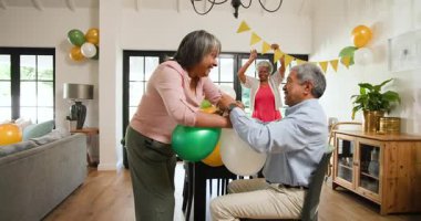 Oturma odasındaki bir doğum günü partisinde balon şişiren üst düzey çok ırklı ve beyaz erkek ve kadın arkadaşlar grubu. Kutlama, doğum günü, parti, son sınıf yaşam tarzı ve arkadaşlık konsepti.