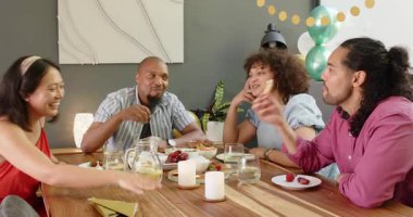 Bir grup mutlu, çok ırklı, siyah ve Çinli erkek ve kadın arkadaş oturma odasındaki bir hoş geldin partisinde yemek yiyip sohbet ediyorlar. Kutlama, parti, yaz ve arkadaşlık konsepti.