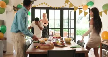 Bir grup mutlu, çok ırklı, beyaz ve Hintli erkek ve kadın arkadaş güneşli oturma odasında sarılıp kutluyorlar. Kutlama, doğum günü, parti, yaz ve arkadaşlık kavramı.