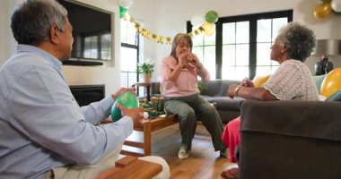 Oturma odasındaki bir doğum günü partisinde balon şişiren üst düzey çok ırklı ve beyaz erkek ve kadın arkadaşlar grubu. Kutlama, doğum günü, parti, son sınıf yaşam tarzı ve arkadaşlık konsepti.