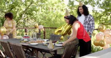 Bir grup mutlu, çok ırklı, siyah ve Çinli erkek ve kadın arkadaş terasta bir doğum günü partisi için sofra ve dekorasyon hazırlıyorlar. Kutlama, doğum günü, parti, yaz ve arkadaşlık kavramı.