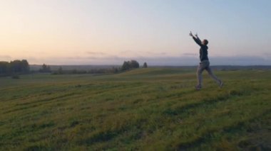 Bir adam elleri ceplerinde durur ve ormanın üzerindeki güzel günbatımını seyreder. Doğanın ve günbatımının güzelliğini düşünüyorum. Büyük yeşil bir çayır, etrafında bir sürü yeşil alan var..