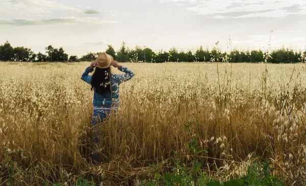 Woman from back with hat in a wheat field, happy woman looking at the horizon in the field