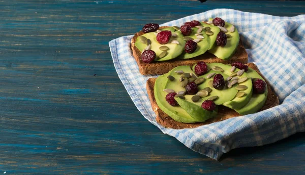 Kırmızı kızılcık ve kabak çekirdeği ve Ayçiçeği tohumları üzerinde mavi ahşap arka plan üzerinde bir mutfak havlusu ile vejetaryen avokado tost